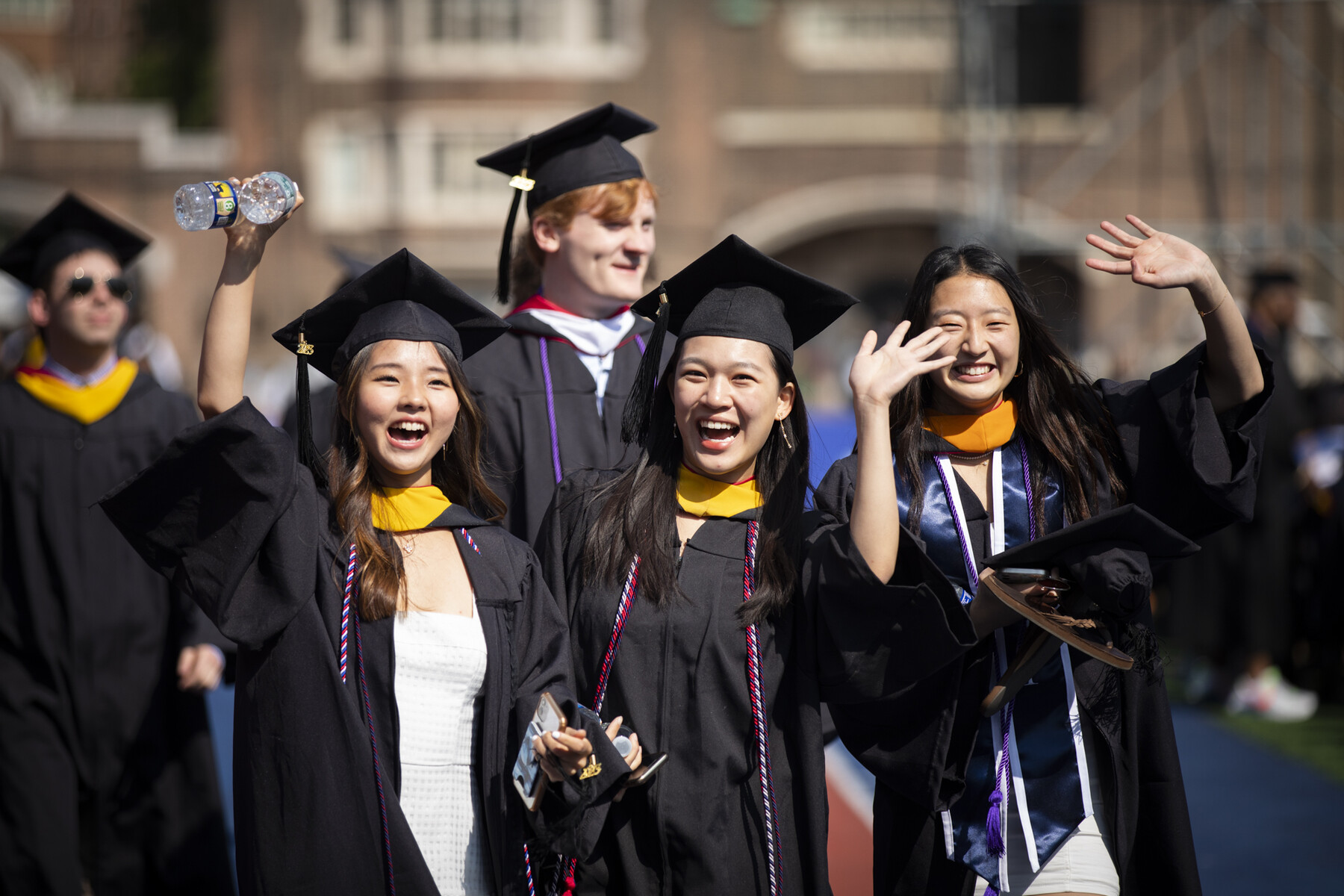 students waving as they enter franklin field during commencement