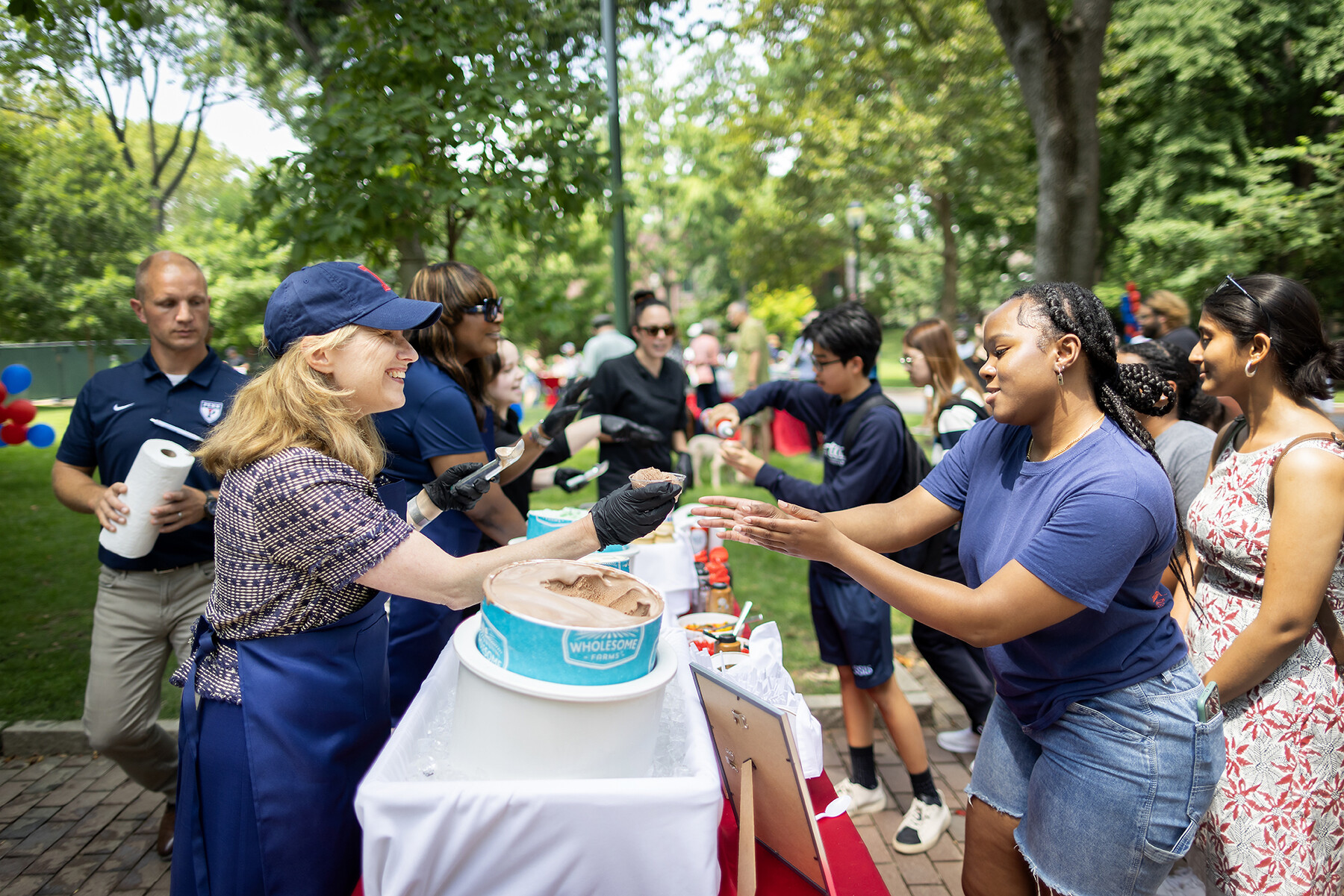 Liz Magill hands a person a cup of ice cream on College Green.
