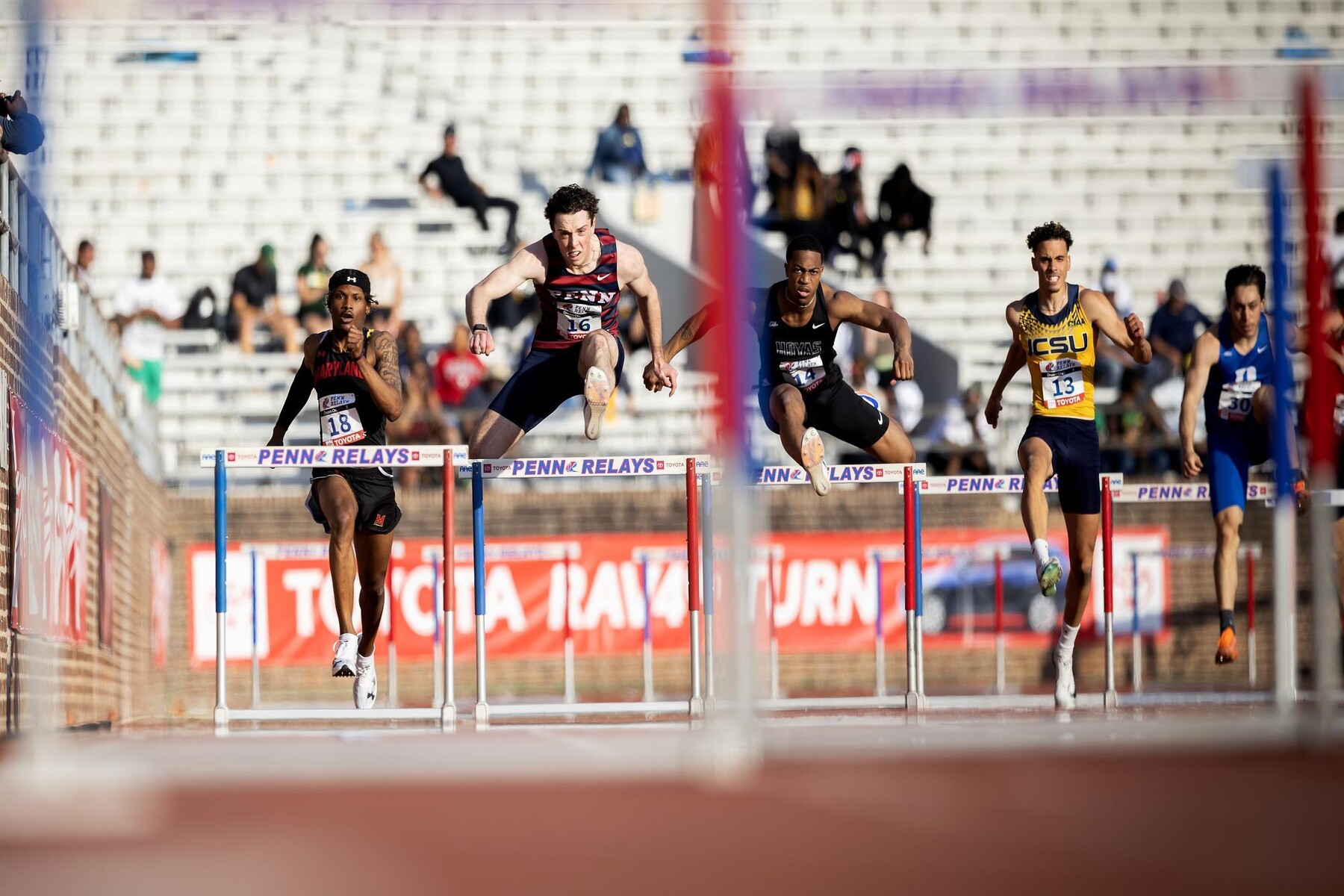 Runners jumping over hurdles at the Penn Relays.