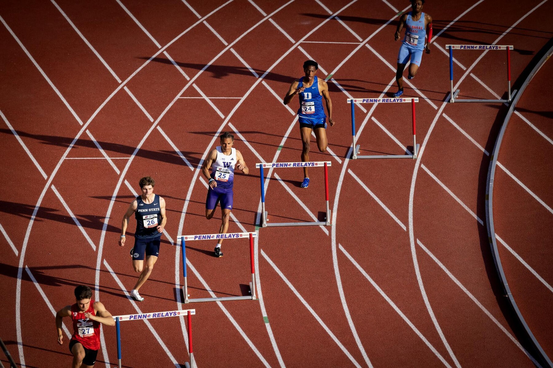 Runners on the track about to run over hurdles.