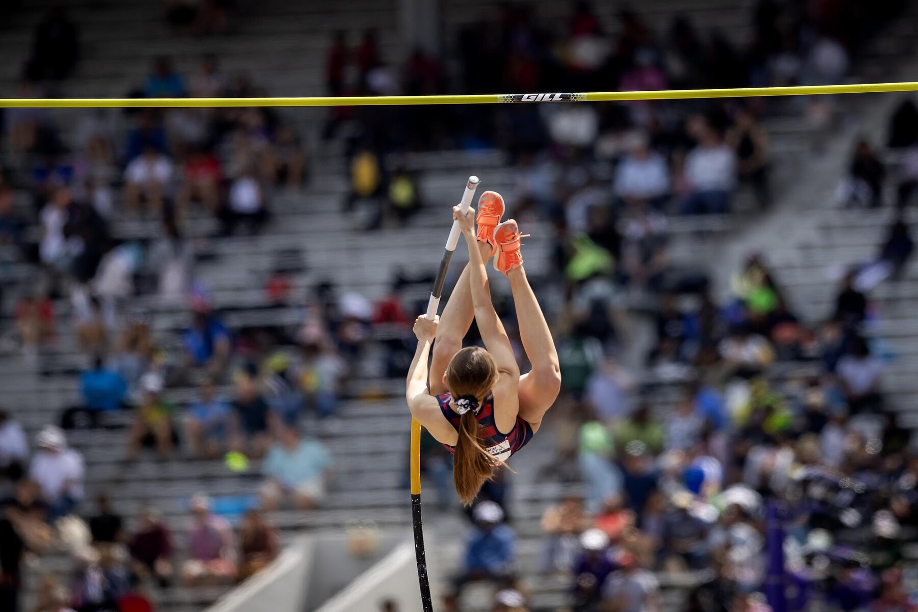 A pole vaulter in mid-jump before the apex of the pole at the Penn Relays.