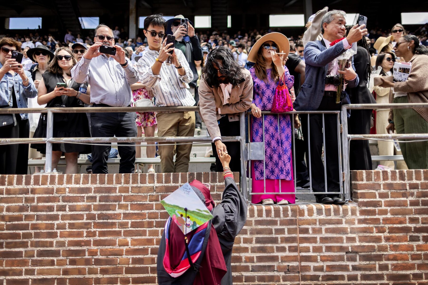 A graduate grabs for the hand of a spectator at the Commencement ceremony on Franklin Field.