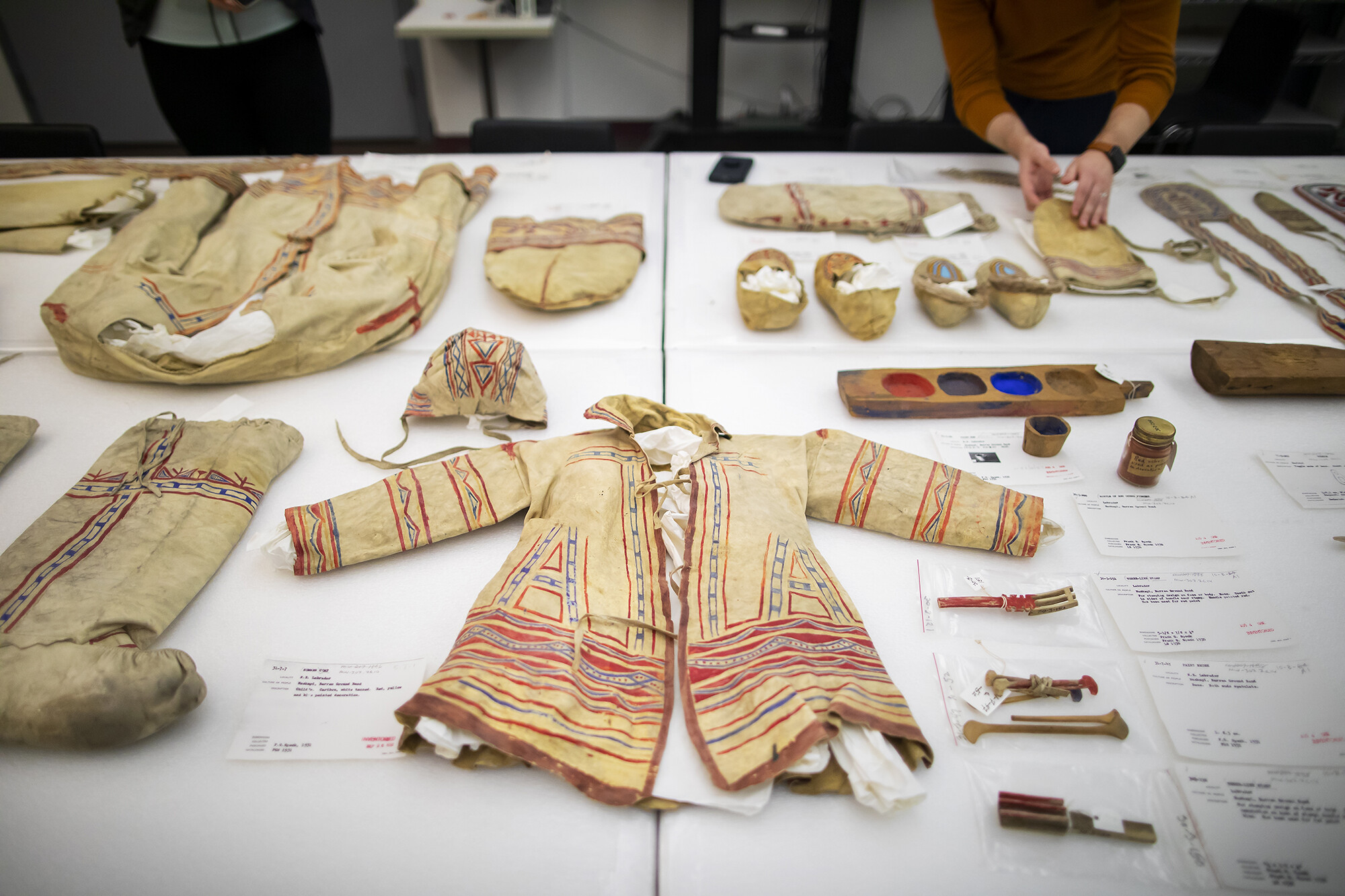 Child's coat and hat on a table surrounded by other objects from the Penn Museum collection.  