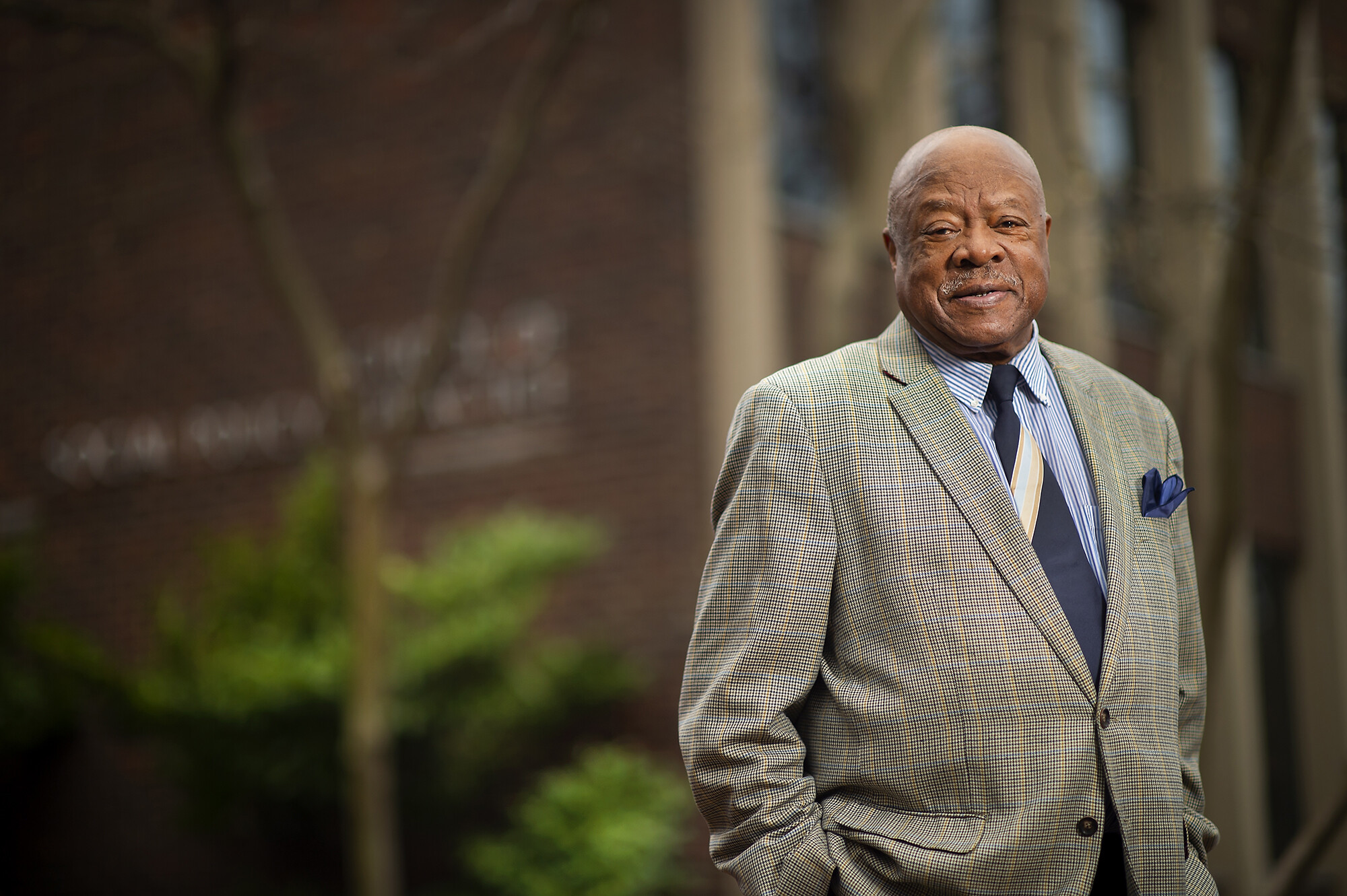 Walter Palmer, wearing a suit and tie, stands with his hands in his pockets outside of Penn's School of Social Policy and Practice.