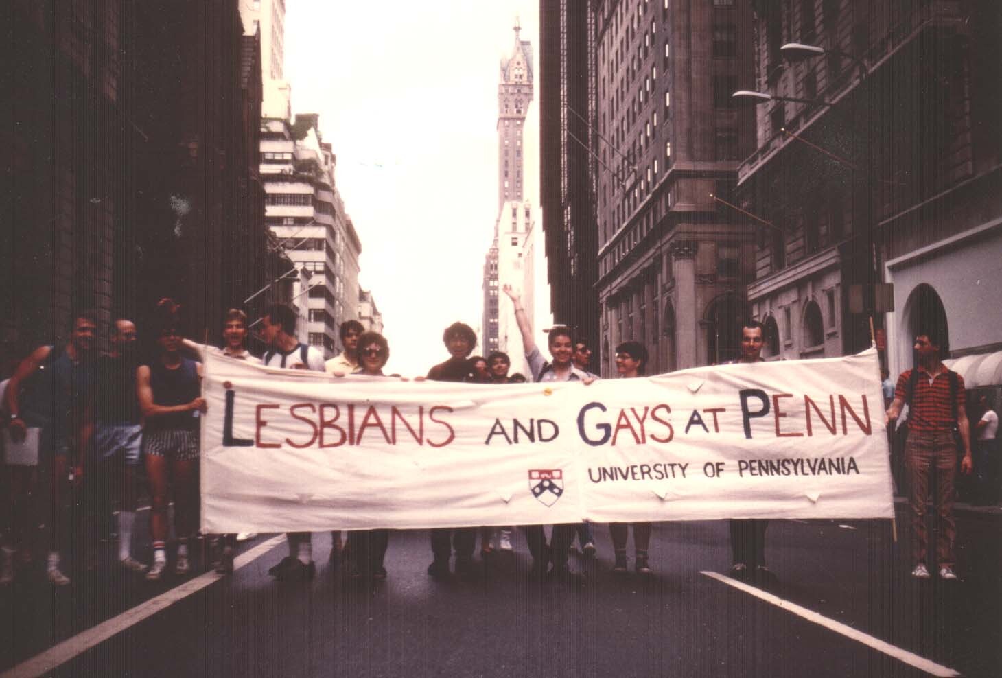 A group of people striding through Center City, Philadelphia carrying a banner that says "Lesbians and Gays at Penn"