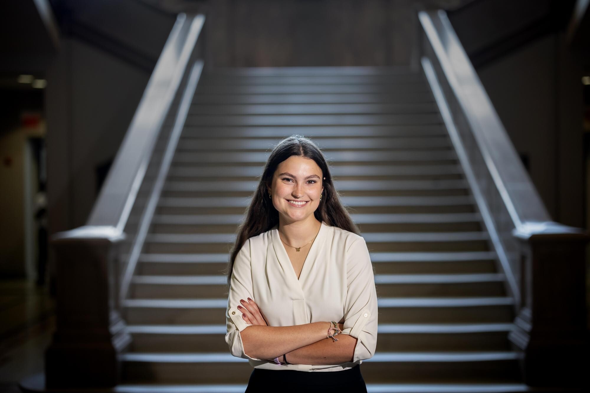 Ella Vance stands in front of a staircase with her arms crossed.