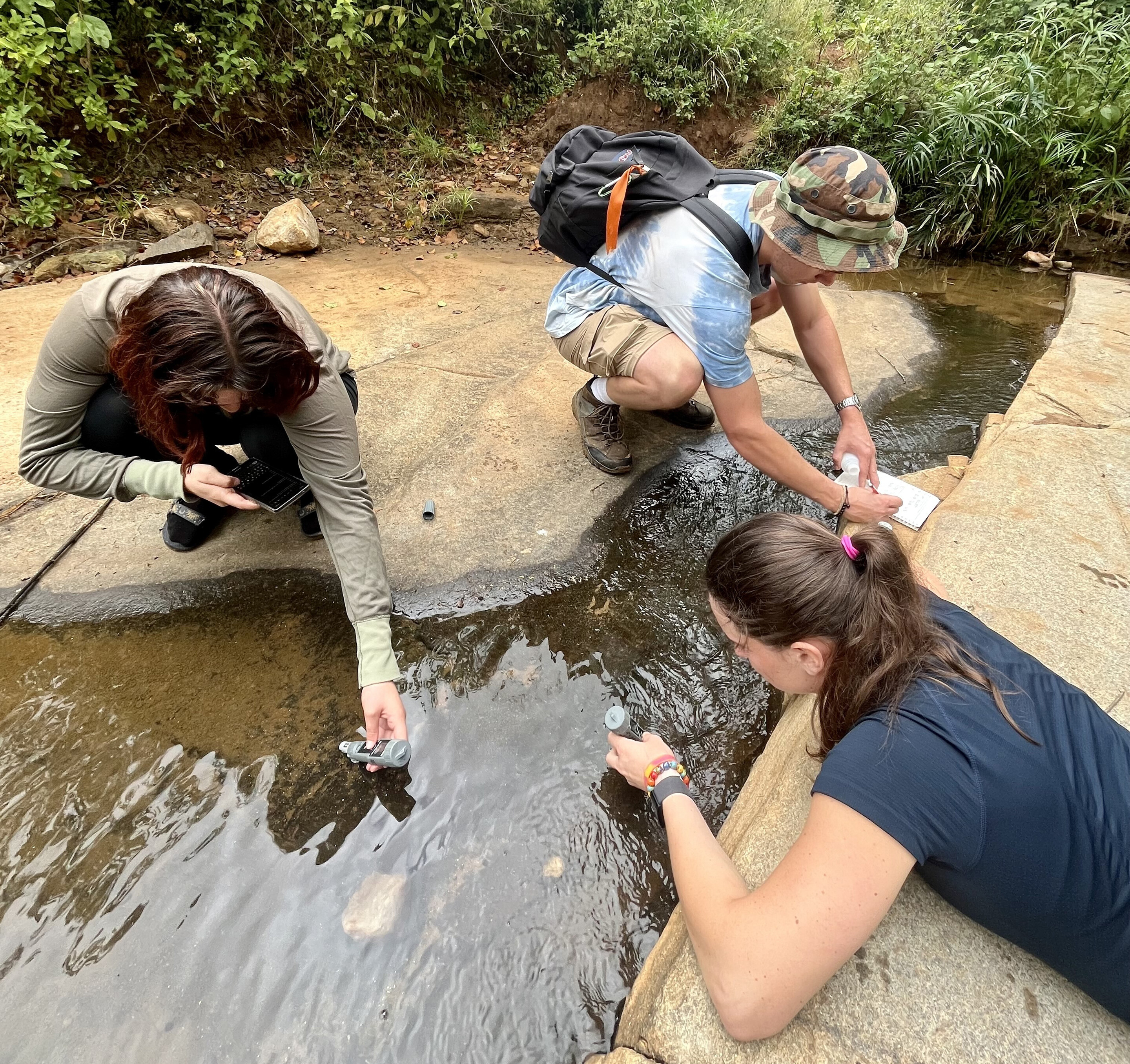 Three people test water below a sand dam.