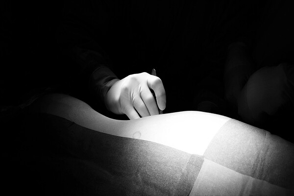 surgeon's gloved hand holding a scalpel under a light