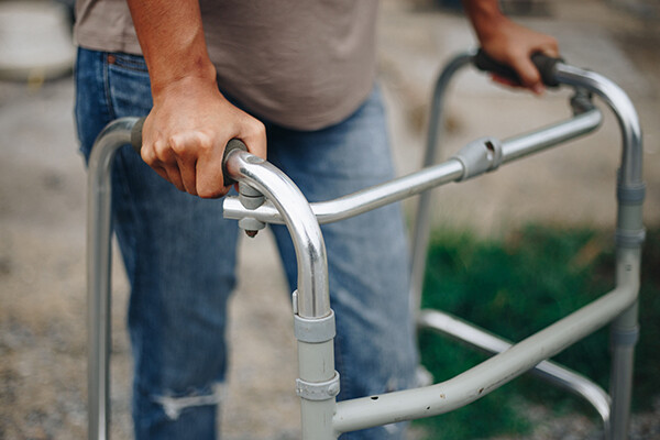Older person’s torso closeup with hands holding onto a walker