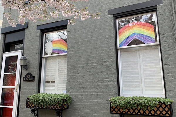 Paper rainbows hanging in windows of a house with a spring blossoming tree branch in front