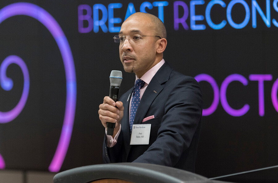 Paris Butler speaks into a microphone while wearing a suit.