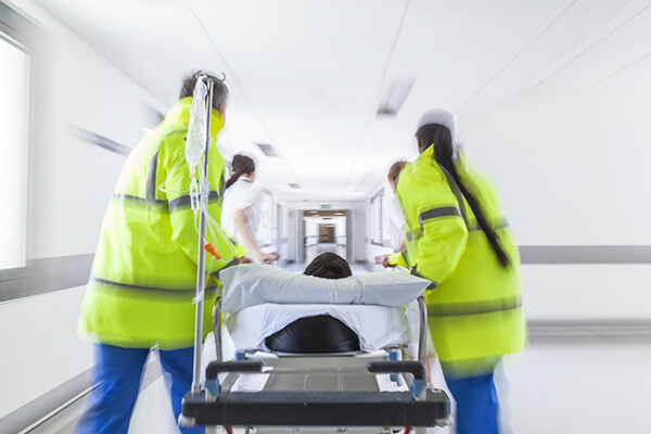 A team of paramedics wheeling in a patient on a gurney into an ER hallway.