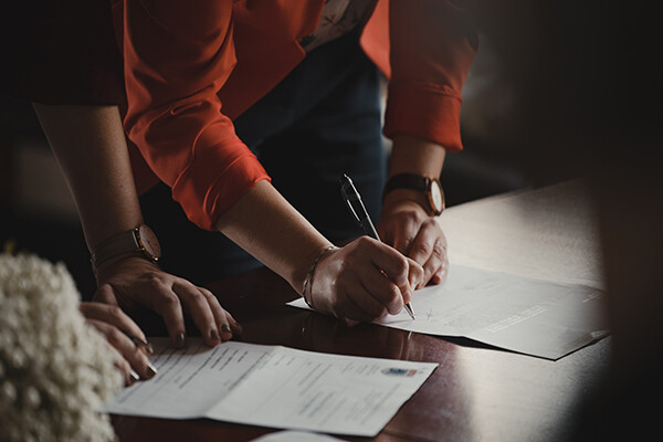 Two people standing over a table signing documents.