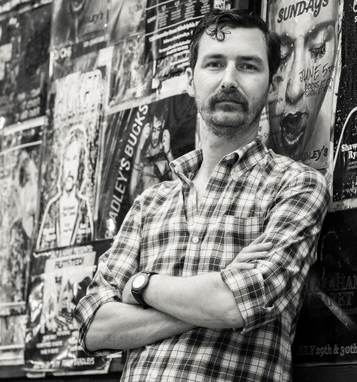 Michael Fichman leaning against a wall covered in flyers. 