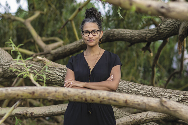 Eugenia South standing in a wooded area with arms folded surrounded by tree branches.