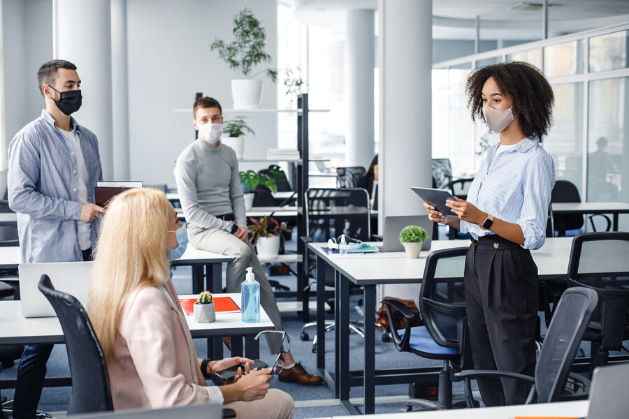 Four coworkers in an office around tables, wearing face masks.