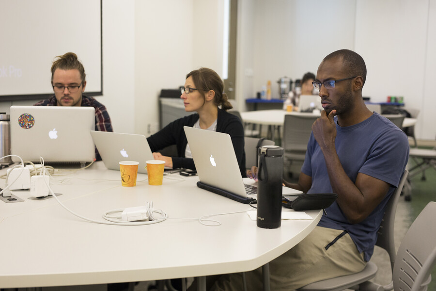 three people working on laptops in a classroom