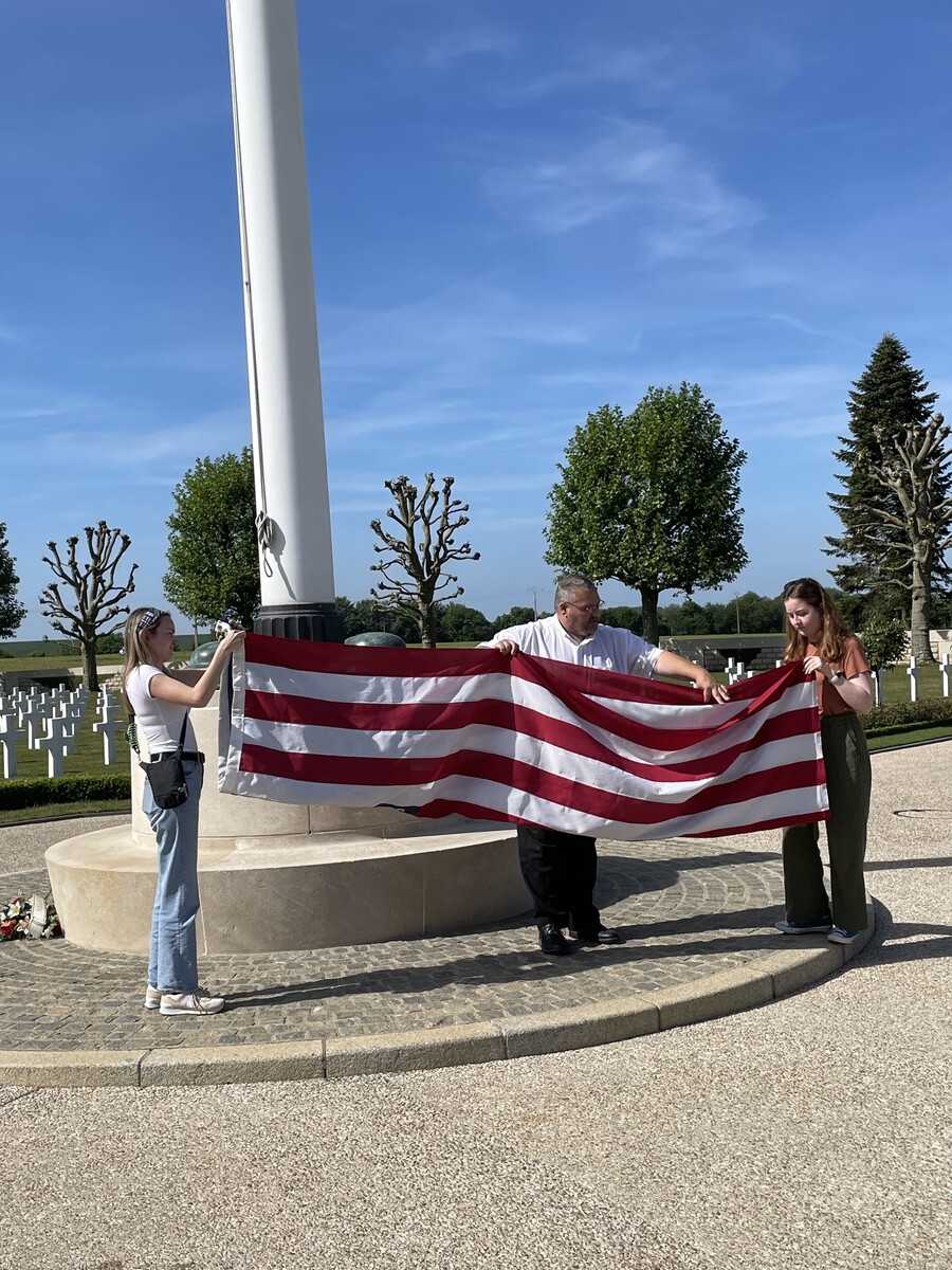 Two students help a French caretaker of an American cemetery in France fold the U.S. flag.