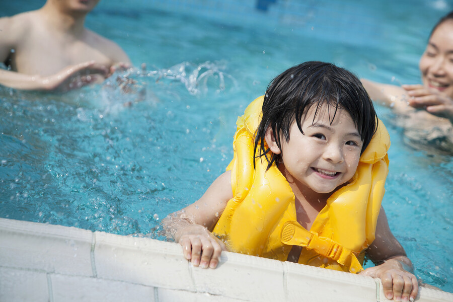 Young child wearing a life vest in the pool with two adults behind them.