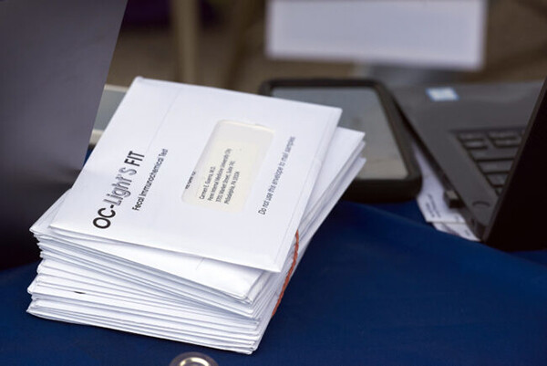 A stack of medical mail beside a cell phone and computer.