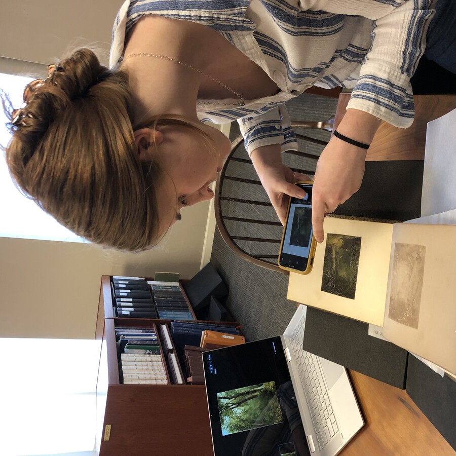 Aili Waller taking a photo with her phone of an artwork in a scrapbook.
