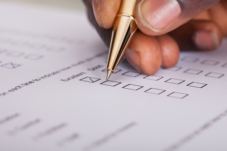 A person’s hand holding a pen filling out a paper survey.