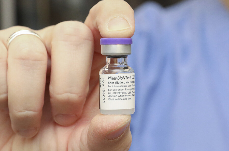 Hand holding a vial of Pfizer vaccine.