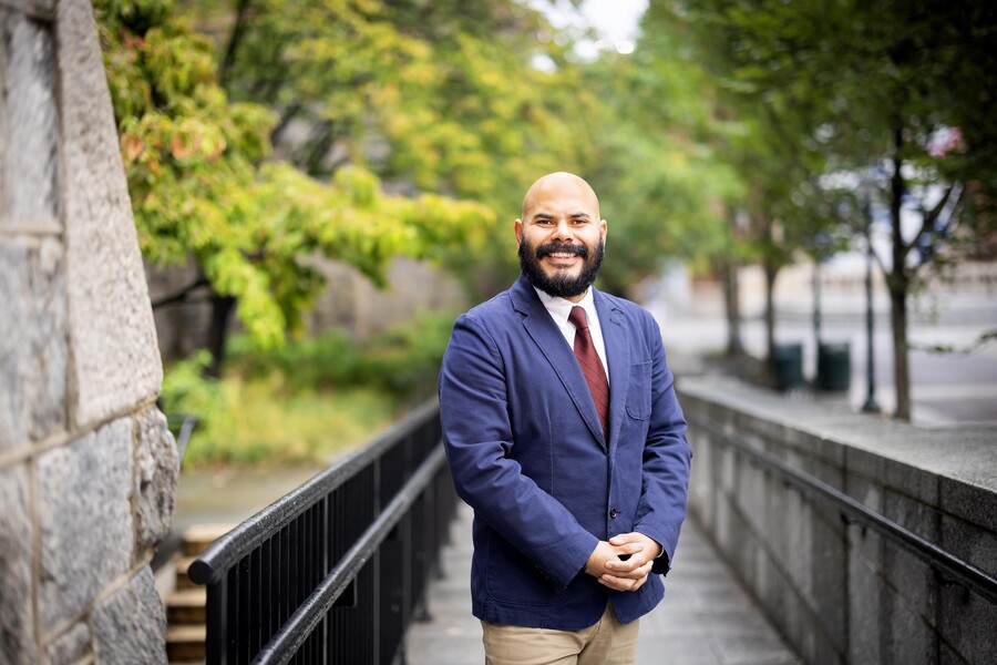 Enmanuel Martínez, the associate director of scholarly and professional development at Penn First Plus, standing and smiling outdoors on a ramp near trees with green leaves
