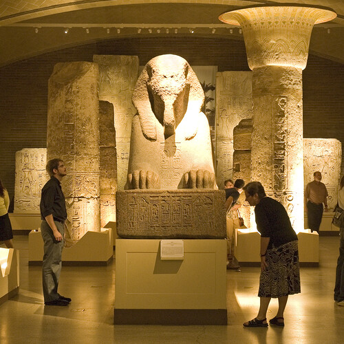 The Sphinx of Rameses II centered at a showroom of Penn Museum with people walking around and looking at the displays.