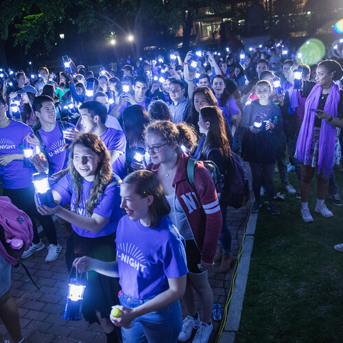 A nighttime, outdoor gathering of a group of students holding small lanterns at U-Night