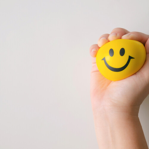 Stress ball with a smiley face, clenched by a hand