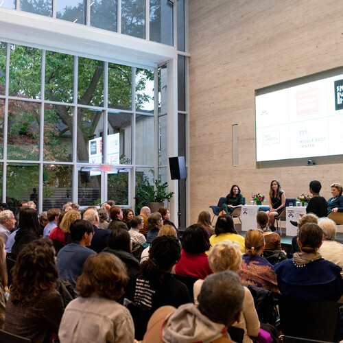 Three people sitting on stage in front of an audience of dozens of people. 