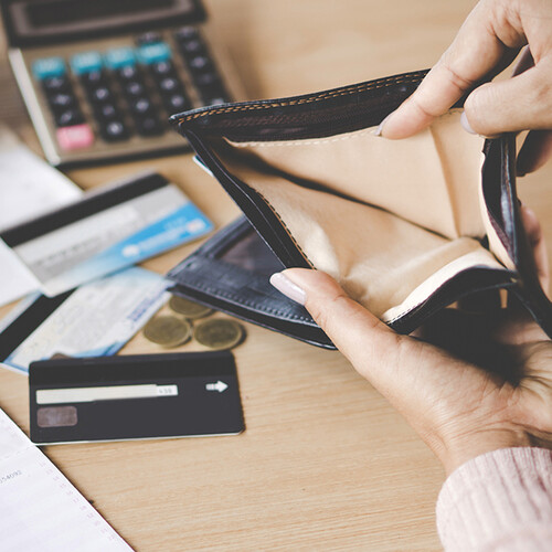 Closeup of a hand holding an empty wallet over a desk strewn with bank statements, credit cards and a calculator.