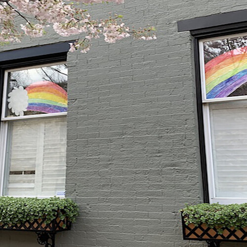 Paper rainbows hanging in windows of a house with a spring blossoming tree branch in front
