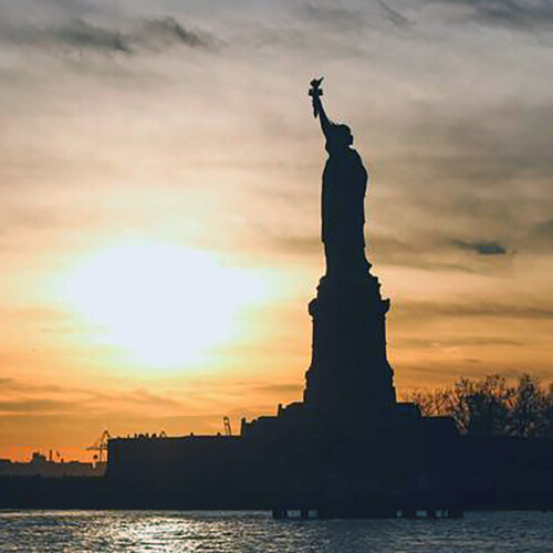 Statue of Liberty in shadow as the sun sets behind