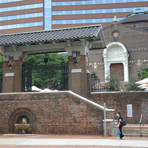 Street view of the exterior entrance of the Penn Museum, a person wearing a face mask is walking past the front staircase.