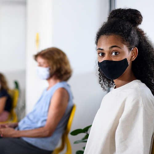 Teenager sitting in waiting room of a clinic wearing a face mask.