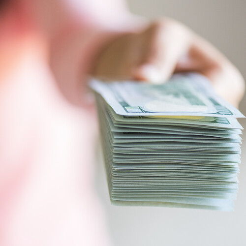 A blurred hand holding a stack of dollar bills, pushing them toward the camera. 