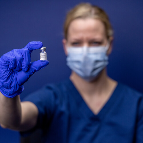 masked health care worker holding bottle of Pfizer COVID-19 vaccine