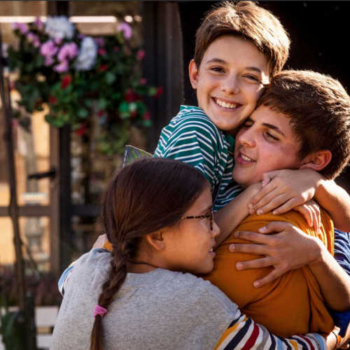 A clip from film Glassboy with three kids cuddled together.
