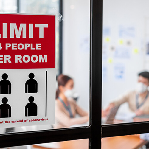 A office room with people wearing mask and a sign hat says "limit 4 people per room." 