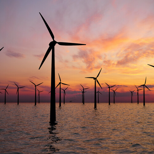 Wind turbines in water, with a sunset in the background. 