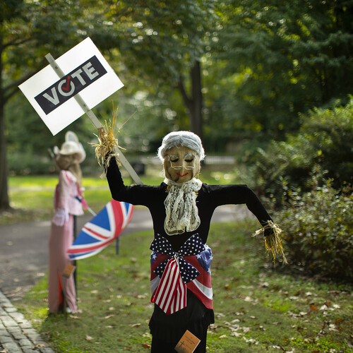Scarecrows holding "vote" sign with a belt in American-flag pattern