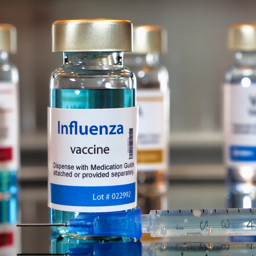 Four bottles of Influenza vaccine beside one medical syringe.