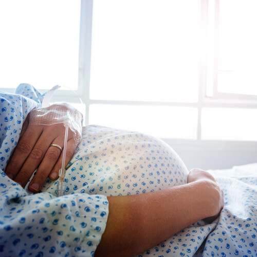 Pregnant person laying in a bed with an IV drip in their arm.