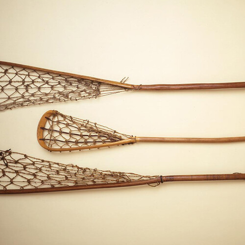 Three lacrosse sticks of differing lengths laid on a flat surface.