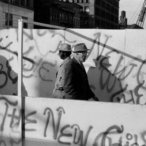 Two people in hats and glasses passing by each other on the street.