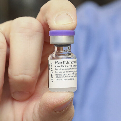 Hand holding a vial of Pfizer vaccine.