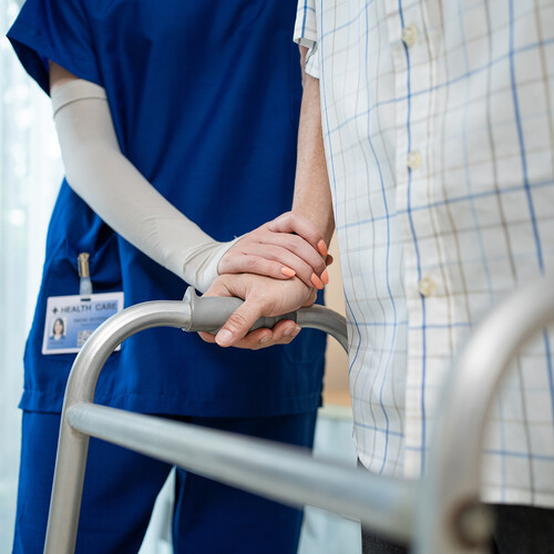 A health care professional with a person walking with a walker.