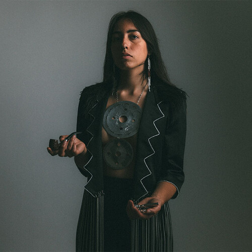 Mali Obomsawin posing in First Nation garb and holding a pipe.